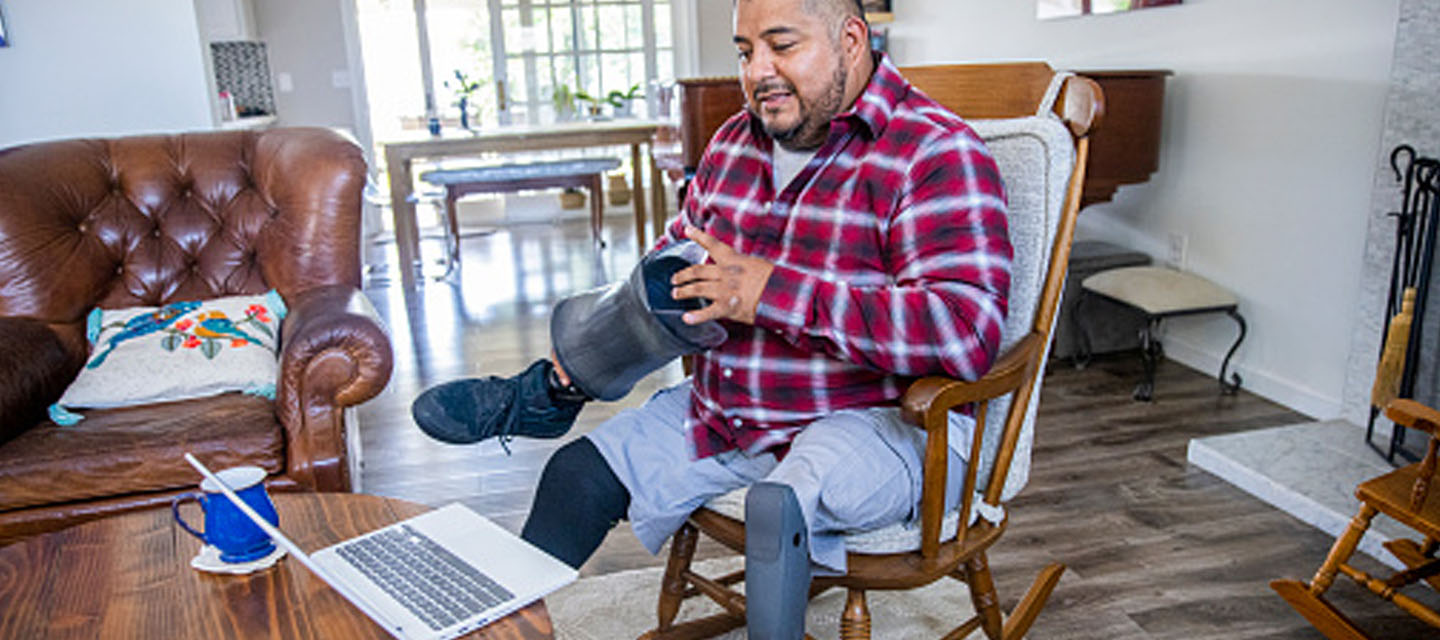 man with a prosthetic leg talking to his healthcare provider virtually with his laptop