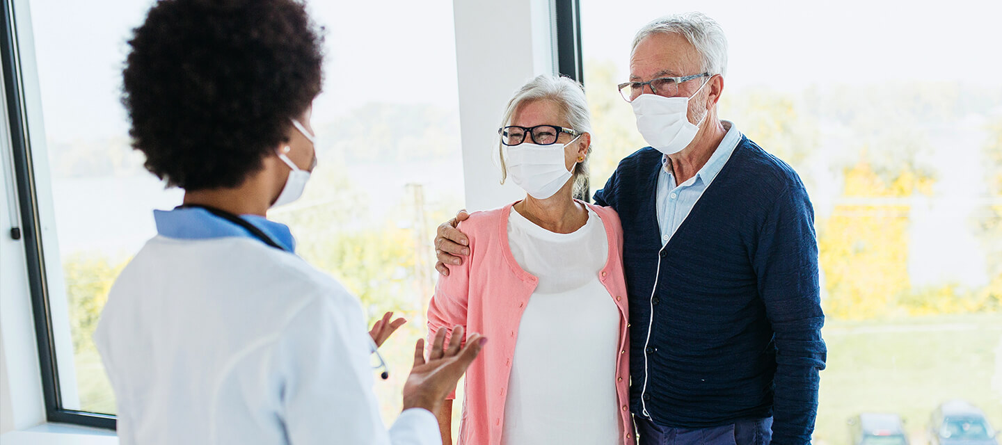 elderly couple wearing protective masks speak with physician