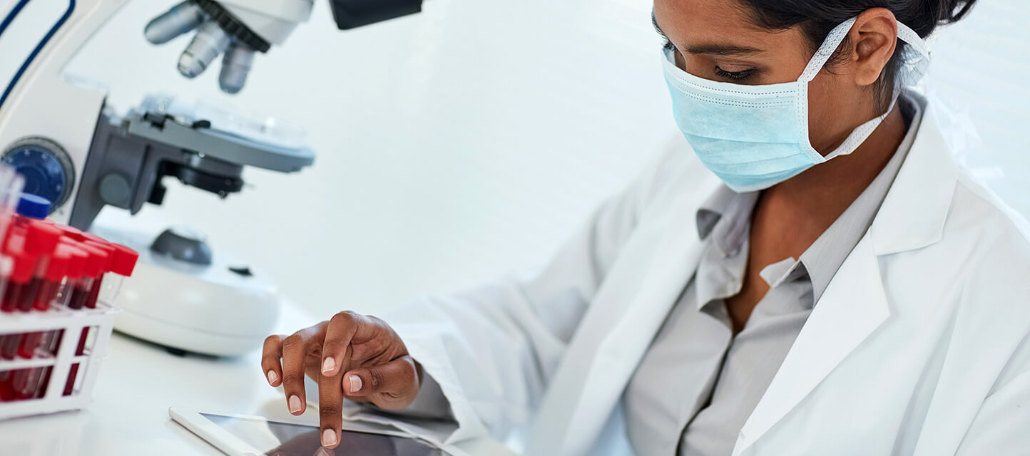 female doctor wearing protective face mask checking blood results on tablet computer