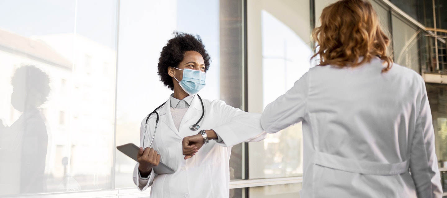 2 physicians wearing protective masks greet each other by bumping their elbows together