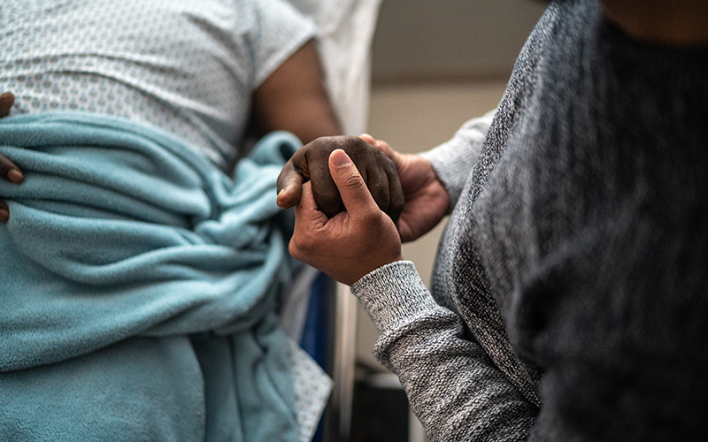 Holding the hand of an elderly patient in a hospital bed