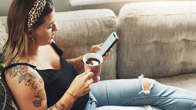 woman checking phone whille on couch having coffee