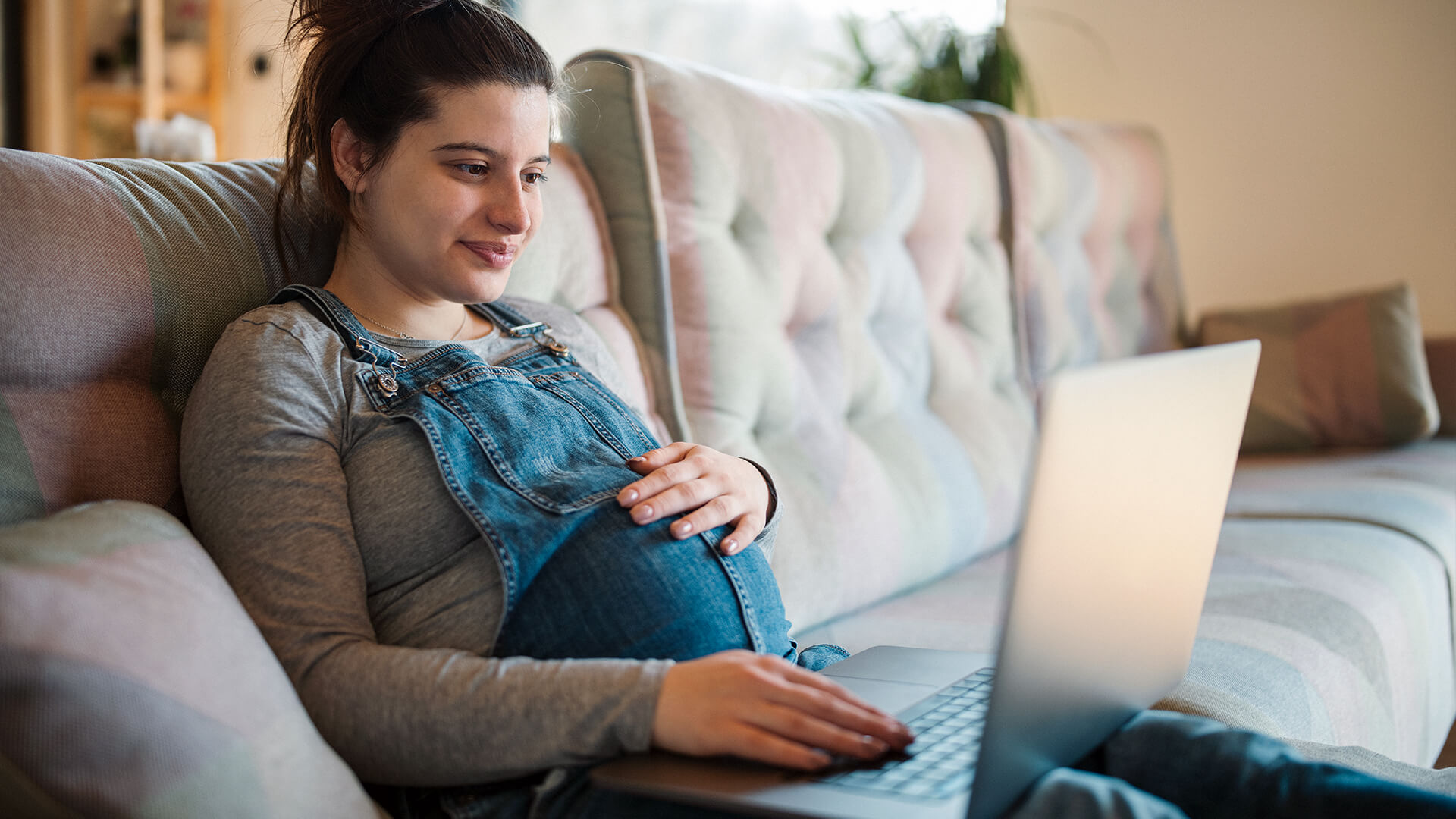 Pregnant woman using a laptop on a couch