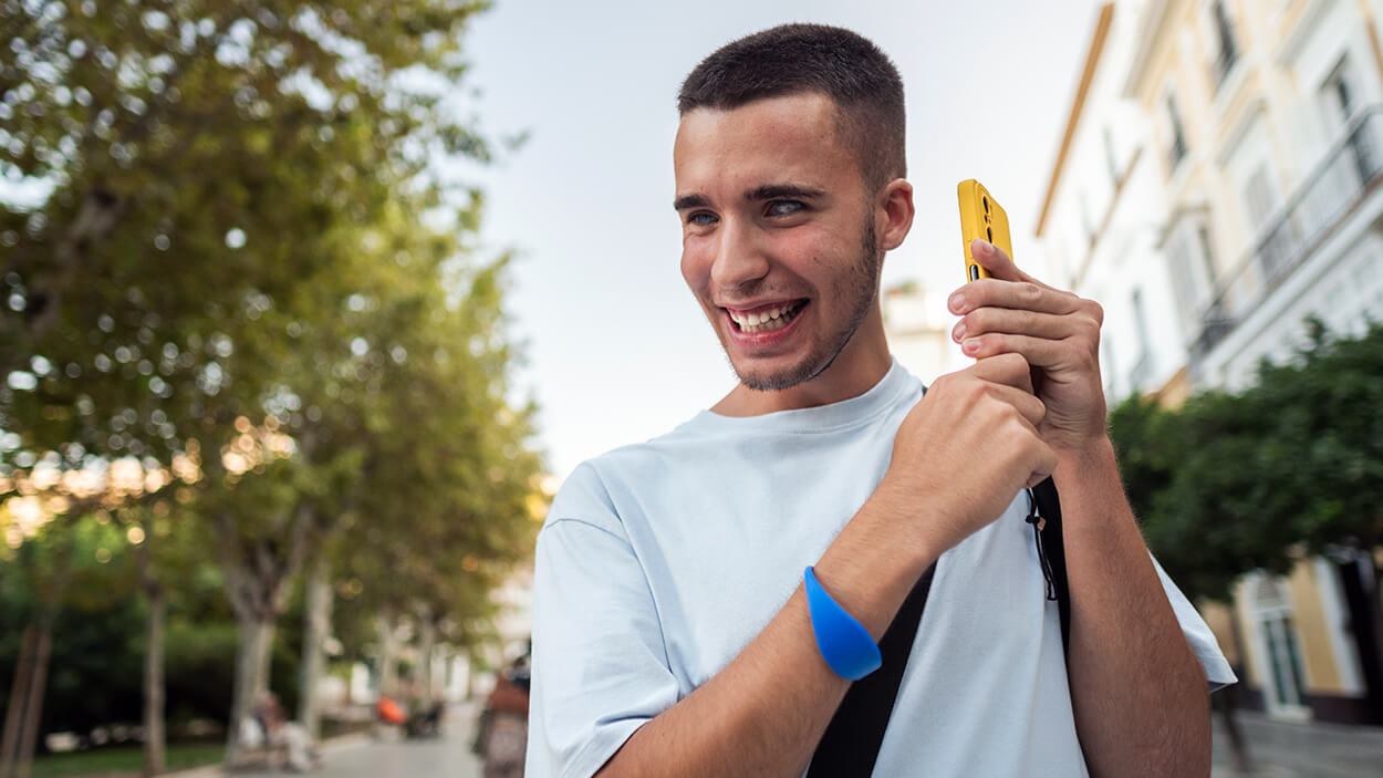 Young blind man smiling and using smartphone outdoors