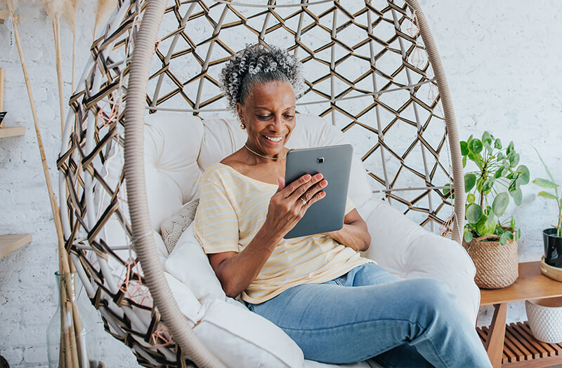 black woman checking tablet at home in big chair