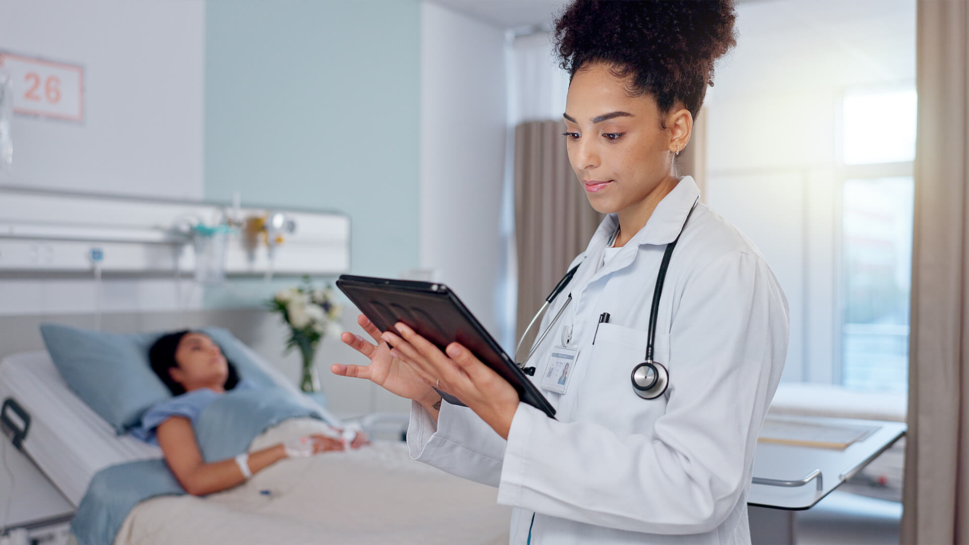 Doctor checking tablet while the patient sleeps in the background