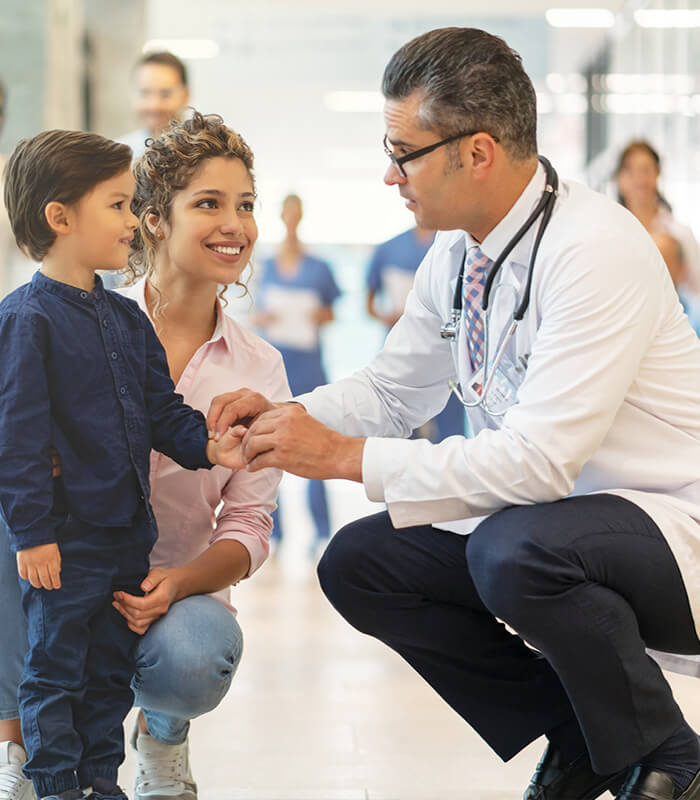 Male physician kneeling to child's level for examination