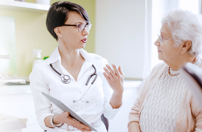 female physician having discussion with elderly patient with digital tablet