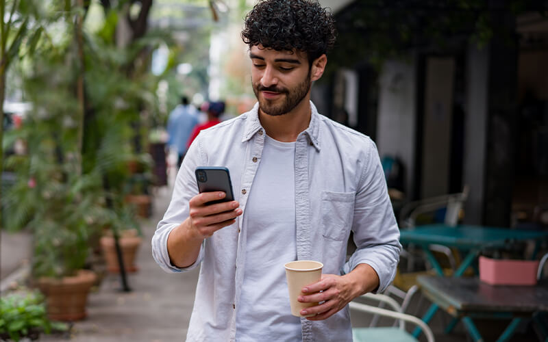 man checking status on phone while grabbing a coffee