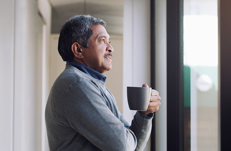Man looking out window while holding a coffee