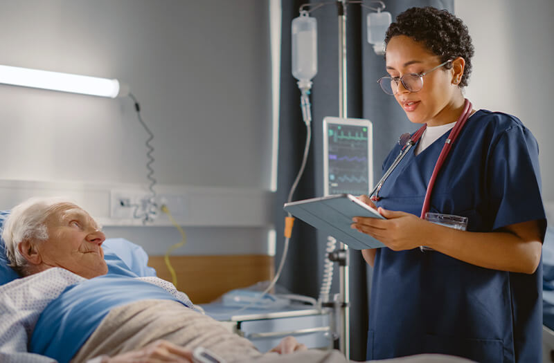 nurse tending to patient bedside with a tablet in hand