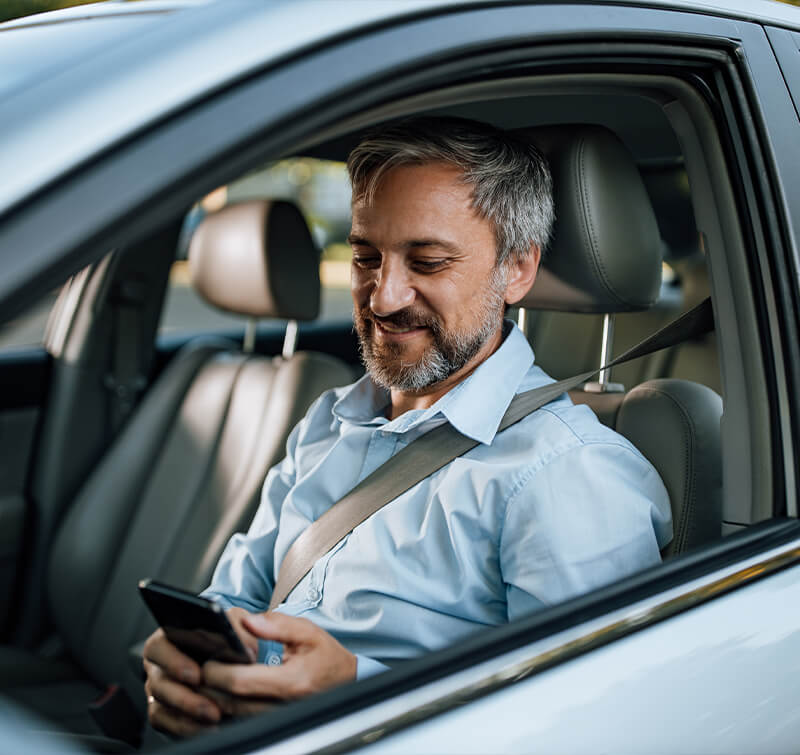 Older hispanic man checking in on phone in car before entering doctor's office