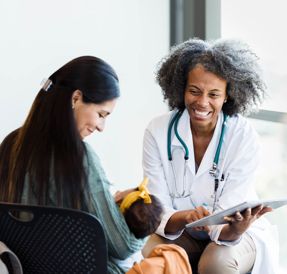 smiling female doctor using tablet while helping mom and newborn